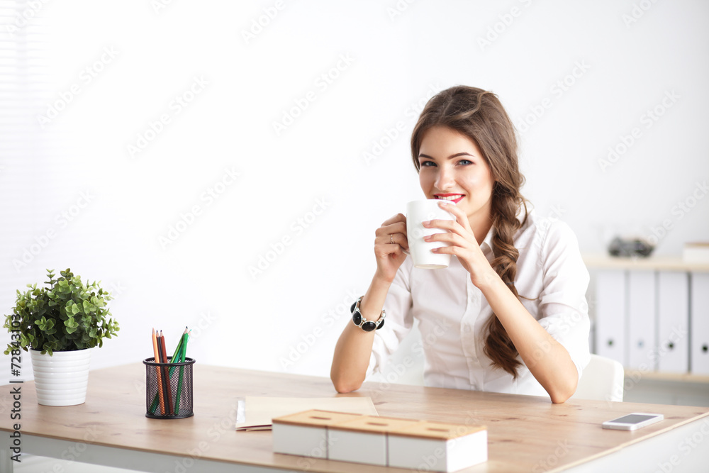 Young businesswoman sitting on the desk with cup in office Young businesswoman sitting on the desk with cup in office
