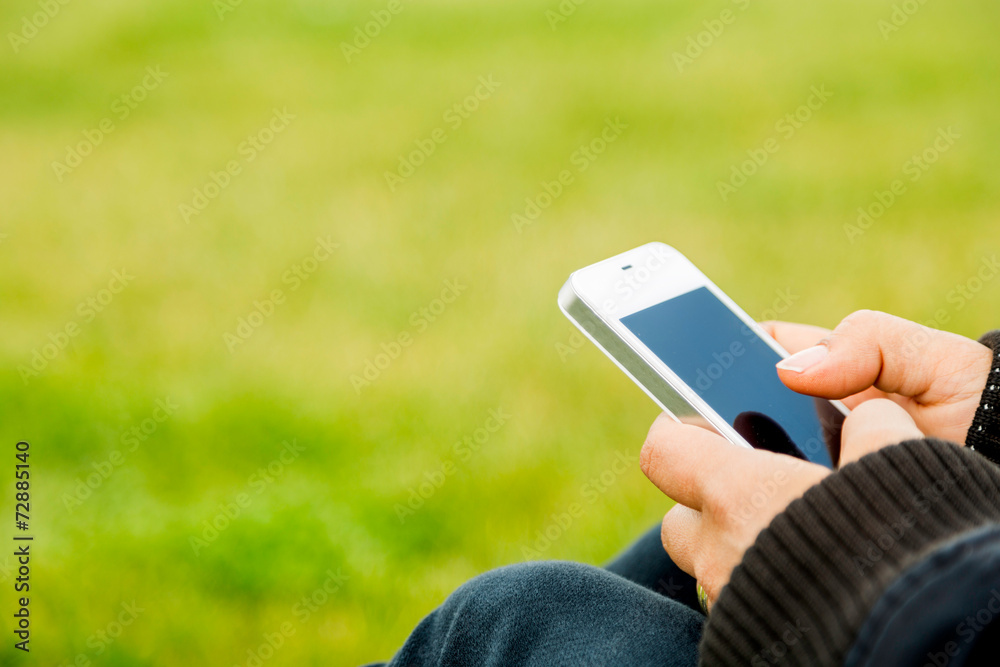 Young woman sitting on grass and using smart phone close-up