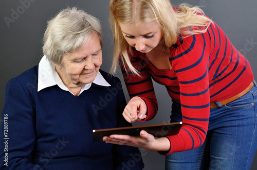 Young woman learns older woman how to use tablet.