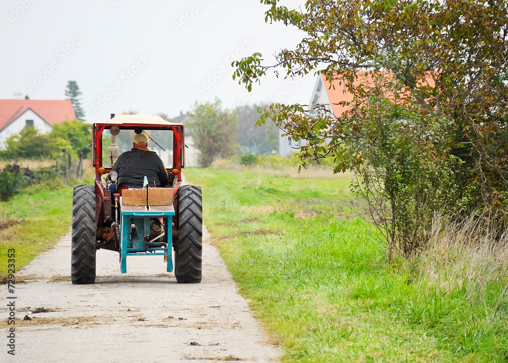 Obraz premium Landwirt fährt mit altem Traktor auf Güterweg