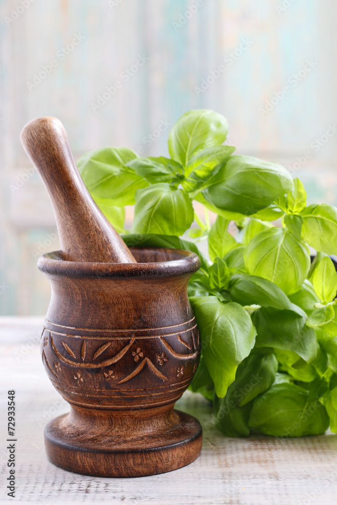 Wooden mortar and basil leaves on the table