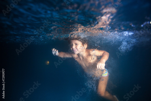 Small boy swimming underwater in pool at night