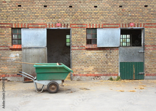 Empty horse stables with dirt wagon on asphalt