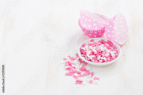colored sugar hearts and paper baking dishes on white wood