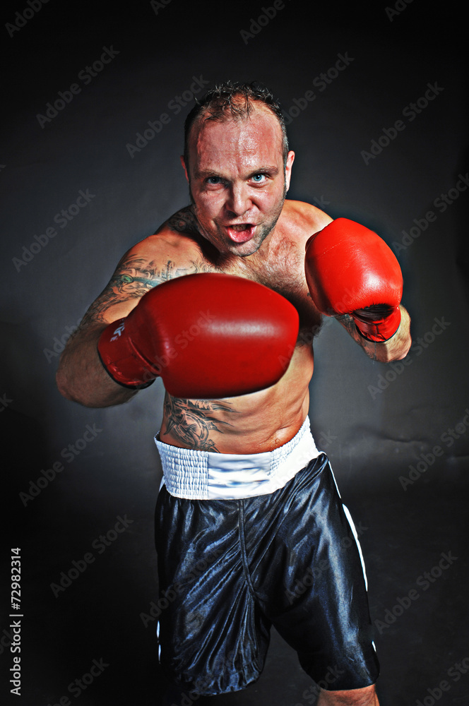 Ein Boxer mit roten Boxhandschuhen schlägt verschwitzt einen rechten haken in Richtung Betrachter Ein Boxer mit roten Boxhandschuhen schlägt verschwitzt einen rechten haken in Richtung Betrachter