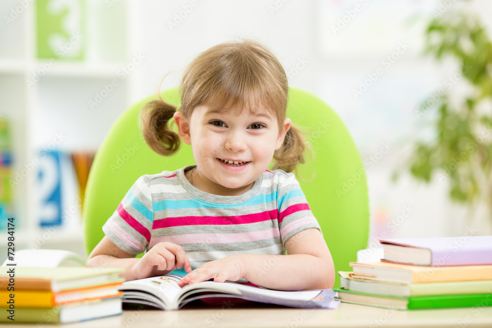 Happy child reading book at table in nursery Happy child reading book at table in nursery