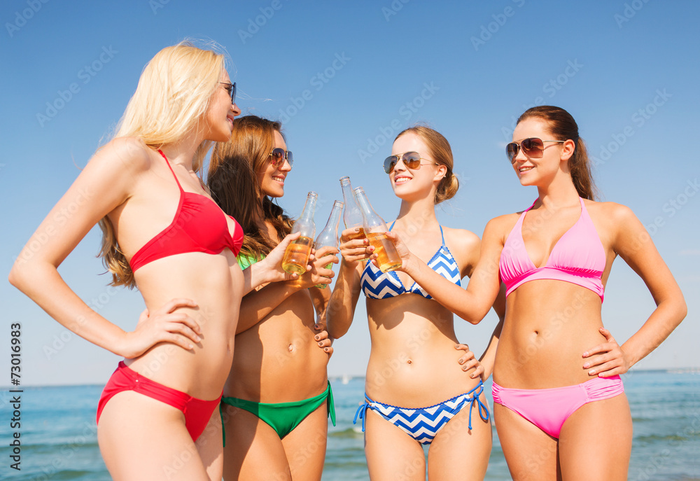 group of smiling young women drinking on beach
