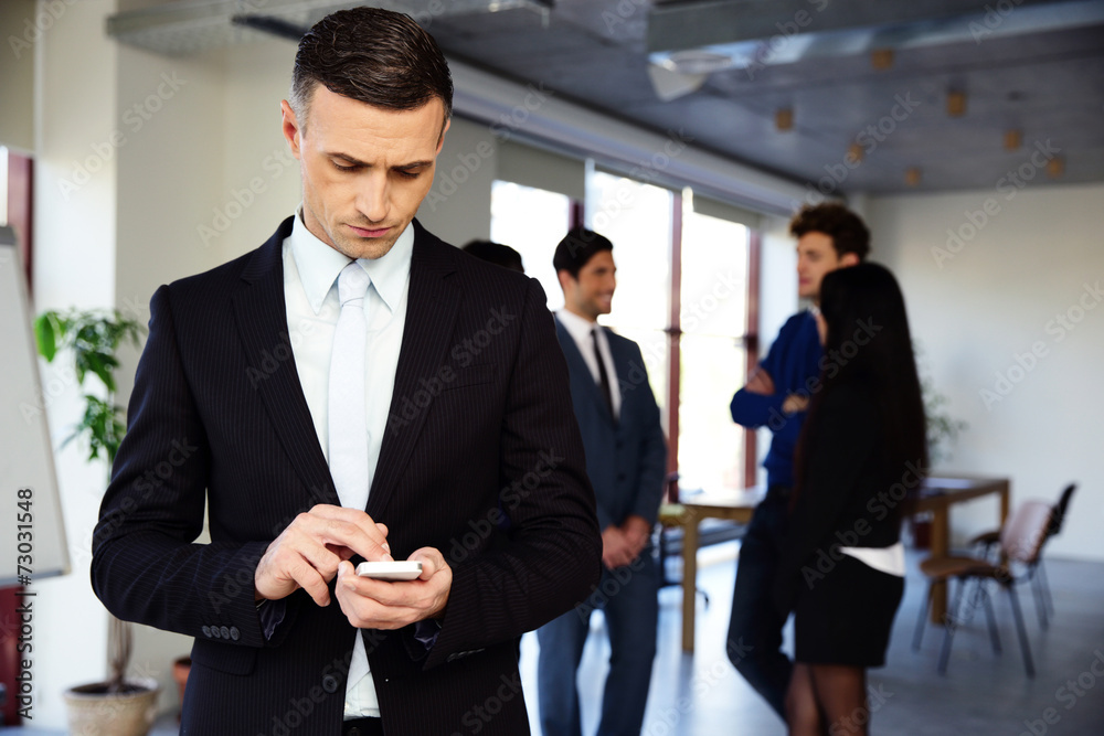 Confident businessman using smartphone in front of a colleagues Confident businessman using smartphone in front of a colleagues