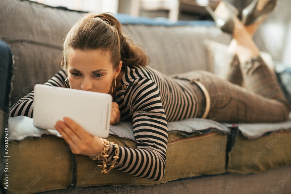 Young woman laying on couch and using tablet pc Young woman laying on couch and using tablet pc