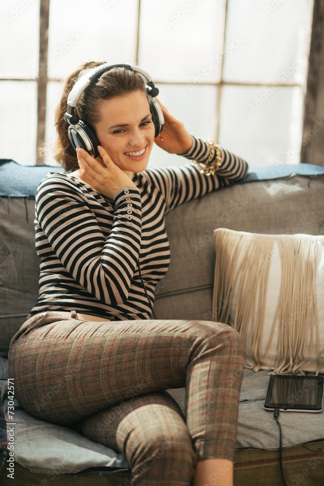 Fototapeta premium Happy young woman sitting on sofa and listening music