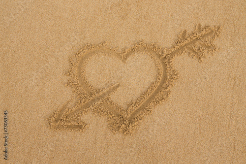 drawing a heart with an arrow on wet golden beach sand