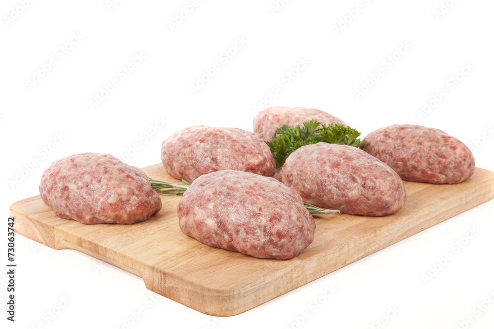 fresh uncooked patties on a wooden board with rosemary and parsl