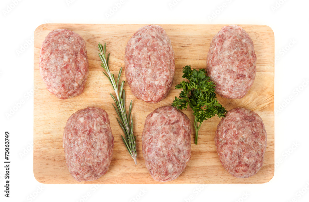 fresh uncooked patties on a wooden board with rosemary and parsl