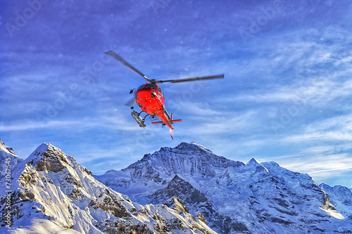 Red helicopter in the sky at swiss alps near in winter