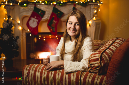 smiling woman sitting on chair at fireplace and drinking tea