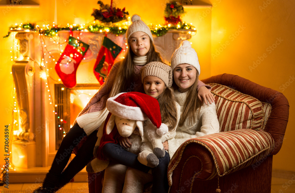 mother and two daughters sitting on sofa at fireplace at Christm