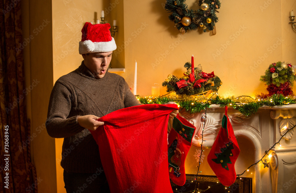 Obraz premium young man in red hat looking inside of Santa bag with amazement