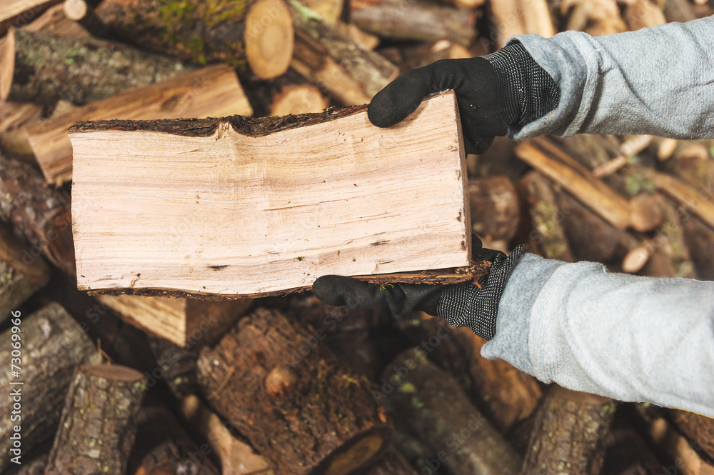 Firewood in a piece of wood stored on the stack, hands holding a Firewood in a piece of wood stored on the stack, hands holding a