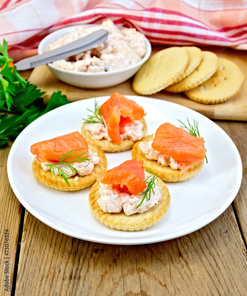 Crackers with cream and salmon in plate on board