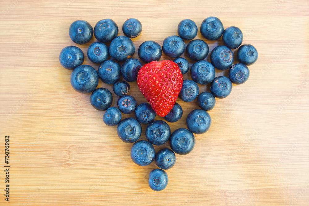 Heart made of blueberries with strawberry in centre Heart made of blueberries with strawberry in centre