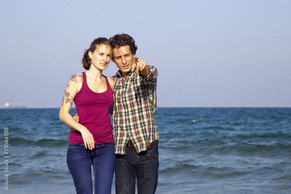 Chico mostrándole algo a su novia en paseo por la playa