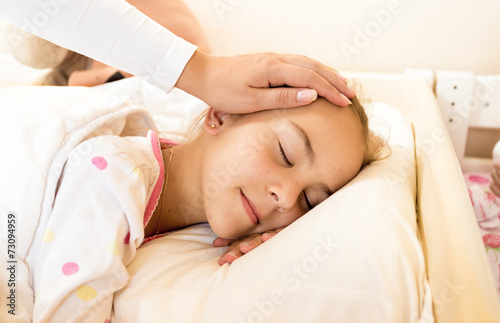 mother holding hand on daughters head at bed