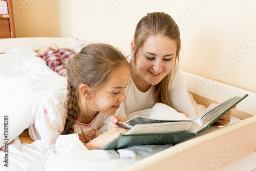 mother reading big old book to daughter at bed
