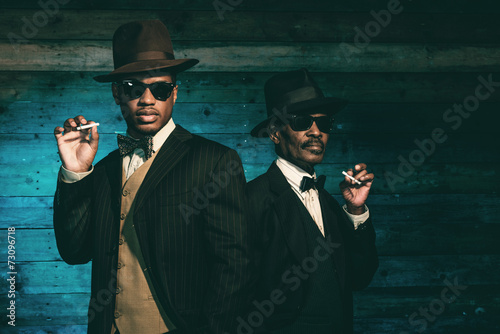 Two vintage african american gangsters smoking cigarette in fron