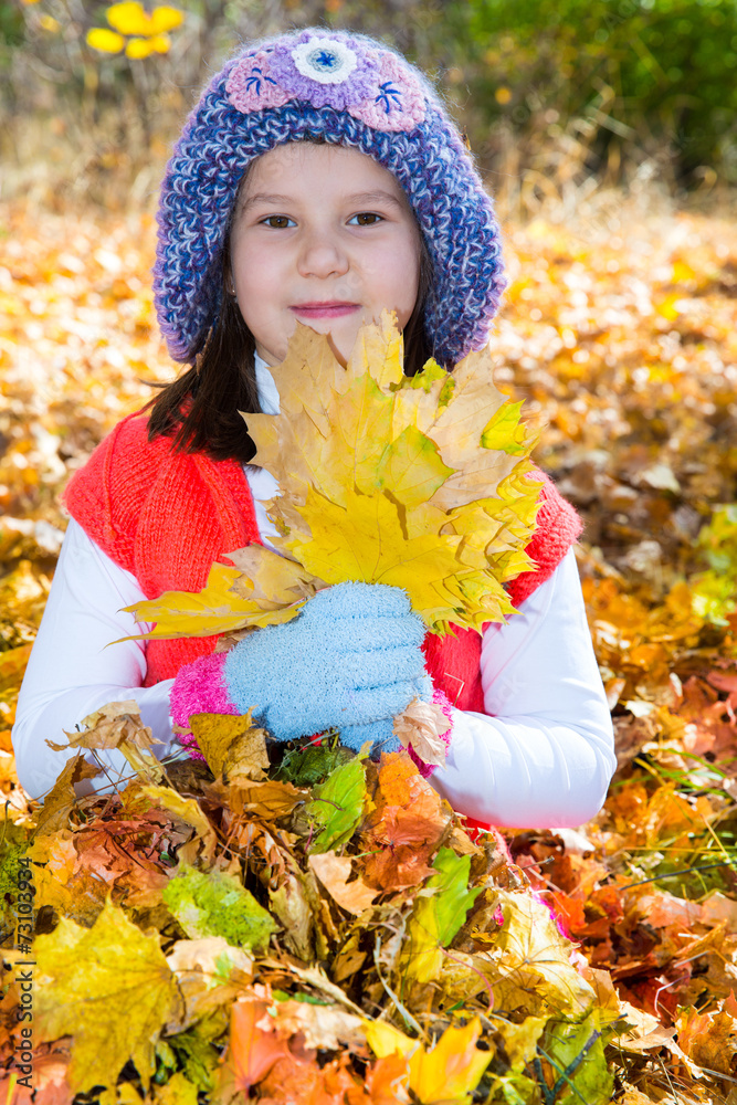 Cute child girl playing with fallen leaves in autumn park