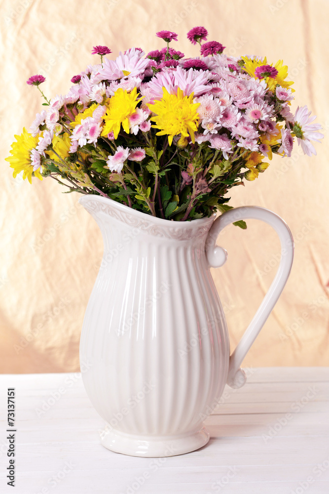 Beautiful flowers in pitcher on table on light background Stock Photo