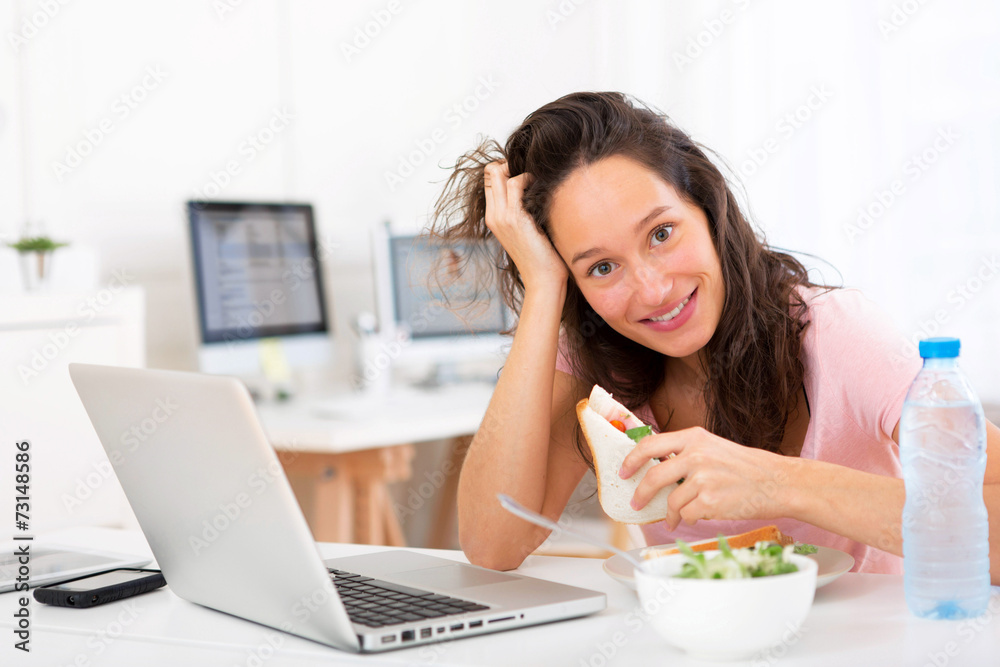 Young attractive student  eating sandwich while working