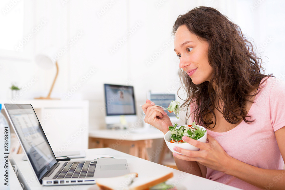 Young attractive student eating salad while working
