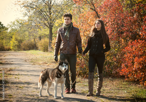 Young couple walking their husky dog in autumn countryside