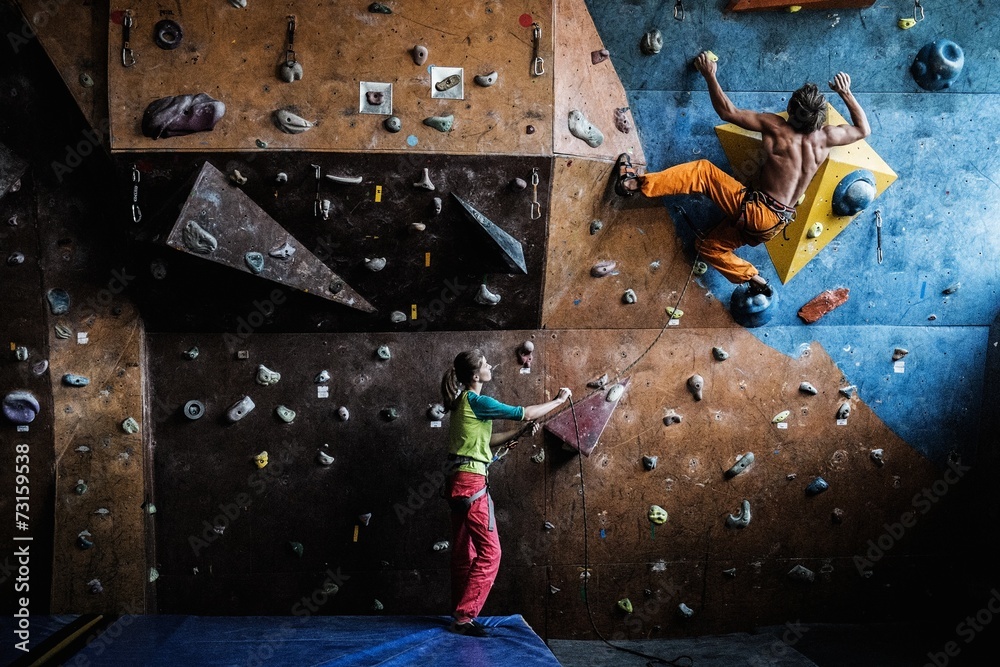 Muscular man practicing rock-climbing on a rock wall indoors