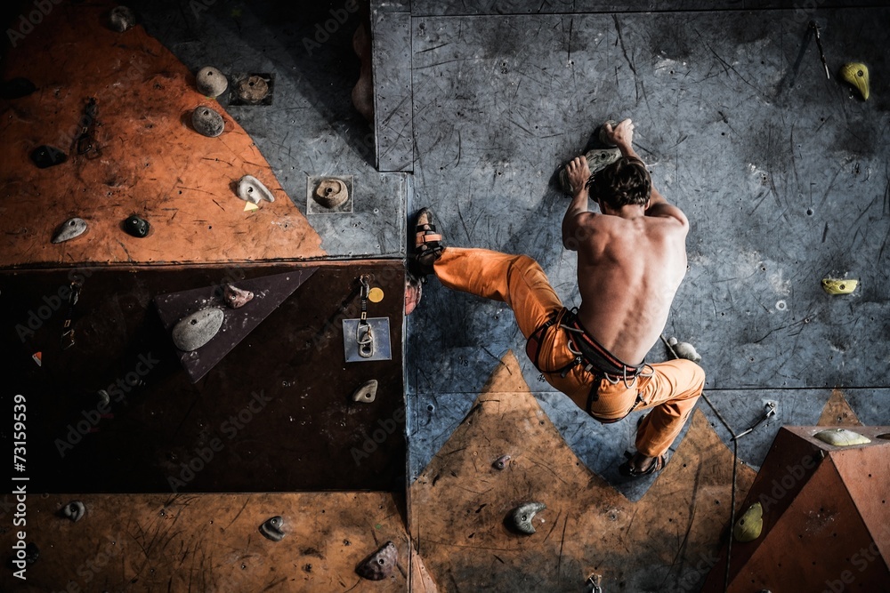 Muscular man practicing rock-climbing on a rock wall indoors - obrazy, fototapety, plakaty 