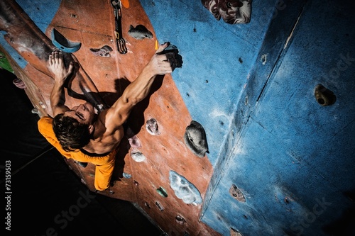Muscular man practicing rock-climbing on a rock wall indoors