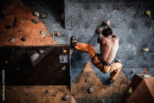 Muscular man practicing rock-climbing on a rock wall indoors photo