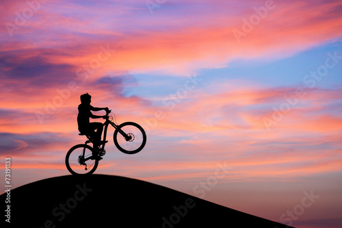 silhouetted mountainbiker doing wheelie in sunset sky on hill © Alex Koch