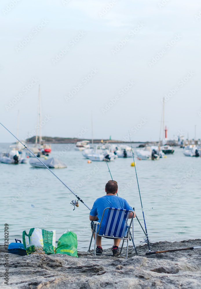 Man fishing in a bay near the boats. Man fishing in a bay near the boats.