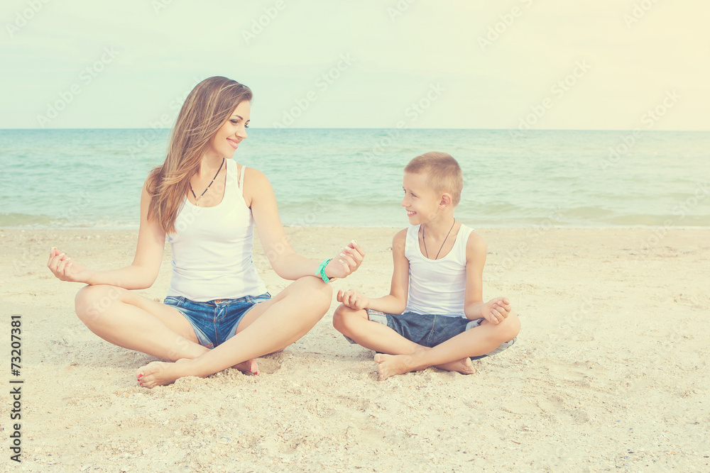 Mother and her son doing yoga on coast of sea on beach.