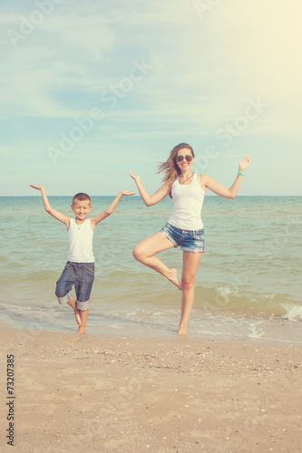 Mother and her son doing yoga on coast of sea on beach.