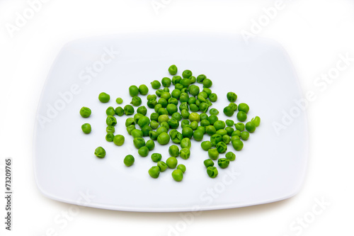 Plate with cooked green peas on a white background