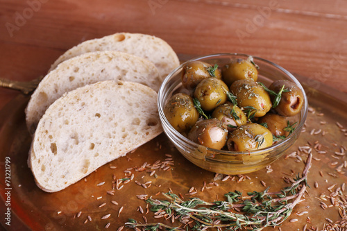 Green olives in oil with spices in glass vase and bread on