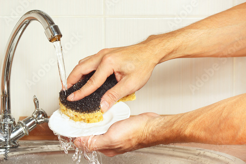 Hands with sponge wash the dirty plate under running water photo