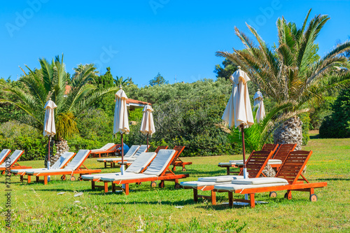 Sunbeds with umbrellas in tropical garden, Sardinia island © pkazmierczak