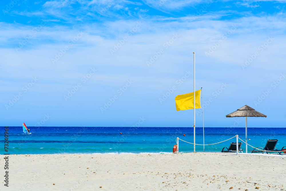 Yellow flag on beach with windsurfer on sea, Sardinia island Yellow flag on beach with windsurfer on sea, Sardinia island
