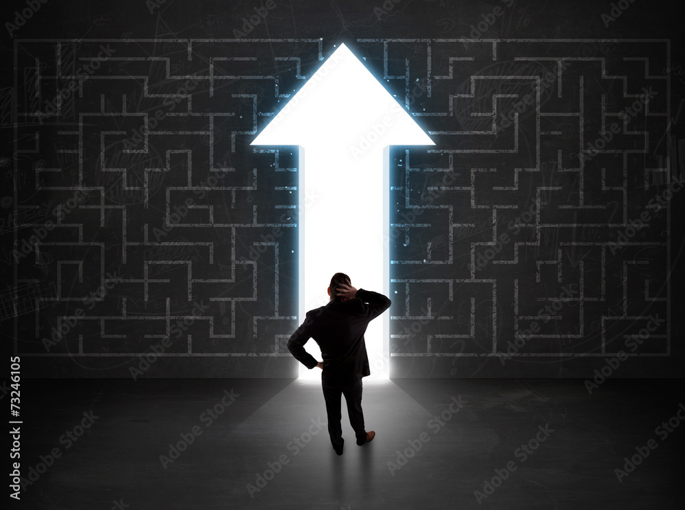 Business person looking at maze with solution arrow on the wall Business person looking at maze with solution arrow on the wall