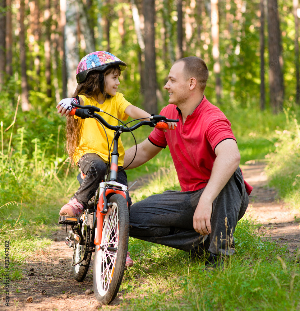 father talking to his daughter, which teaches to ride a bike