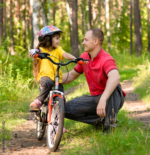 father talking to his daughter, which teaches to ride a bike