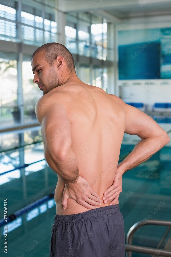 Fototapeta premium Rear view of shirtless swimmer with back ache by pool